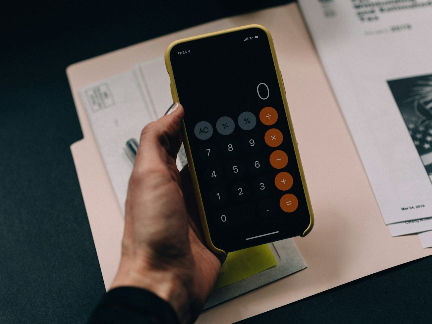 Person holding a smartphone with a calculator app over paperwork